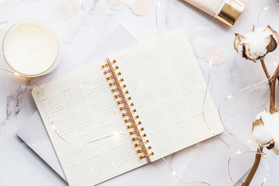 Desktop flatlay items: calendar, candle, garland, cotton flowers lying on marble background 