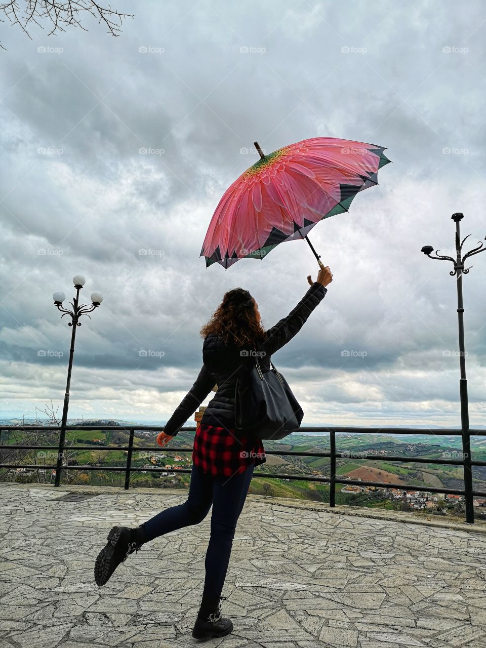 woman from behind plays with pink umbrella in the park on a gray autumn day