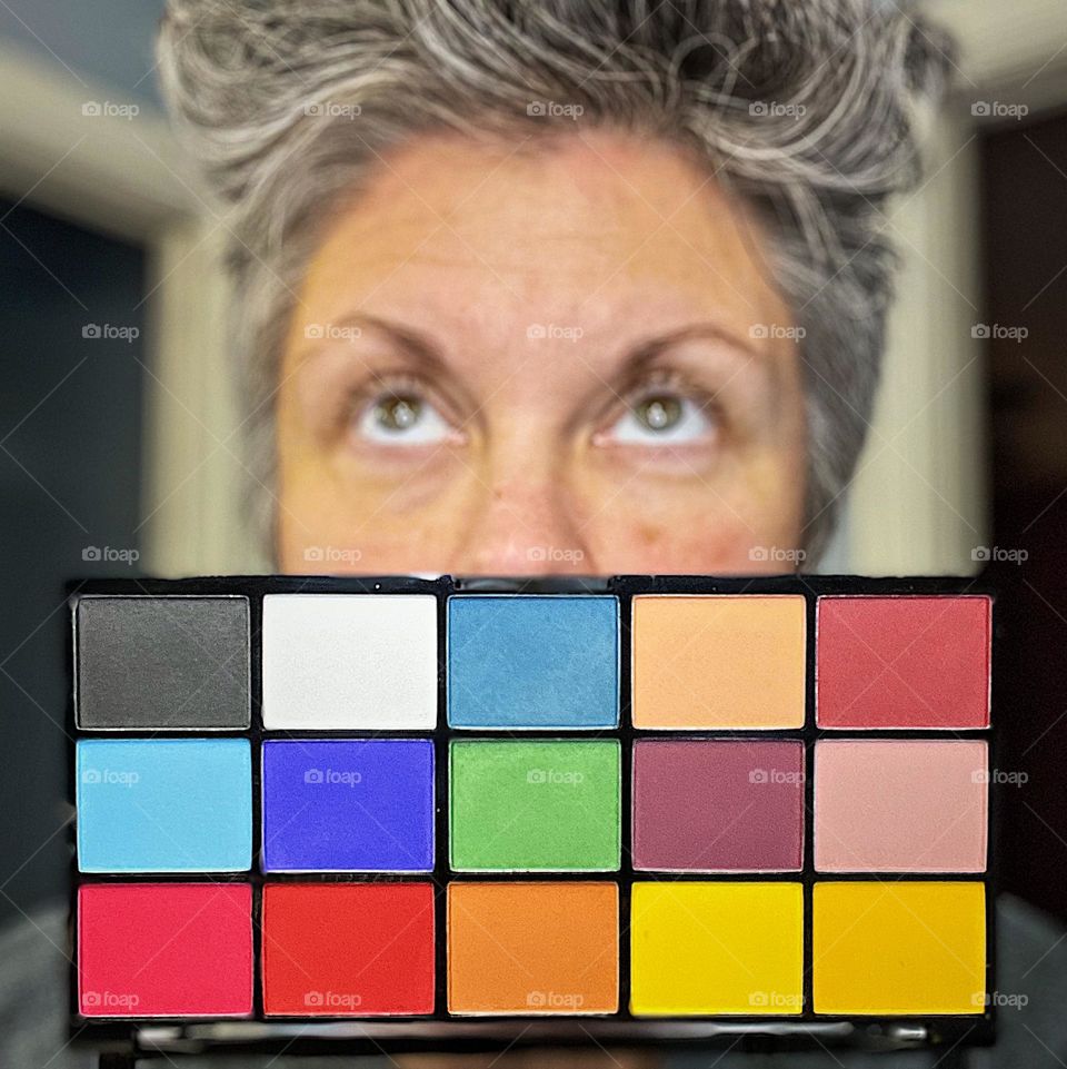 Woman looking up with eye shadow palette, woman looks up in photo, eyes and eye shadow, choosing a color of eye shadow, choices of color, shades of beauty, colorful eyes