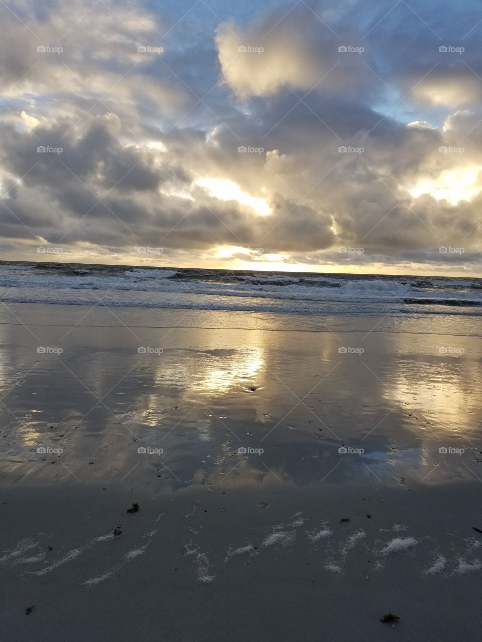 Reflective sky and clouds in sandy beach receding water