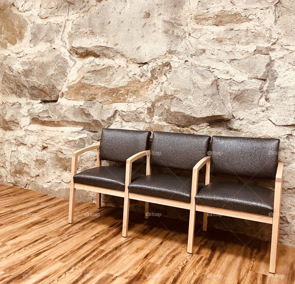 An empty waiting room with simple chairs, a wooden floor, and a raw stone wall. 