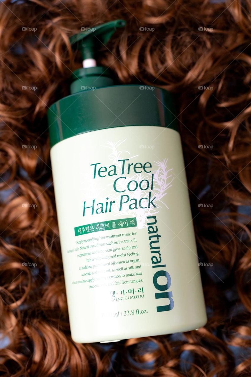 A beautiful, creative view of a large green bottle with a dispenser of a professional hair mask lies in the center on curly hair, a flat lay close-up.