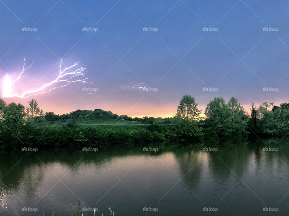 Action shot: bolt of lightening over summer sunset on a lake. 