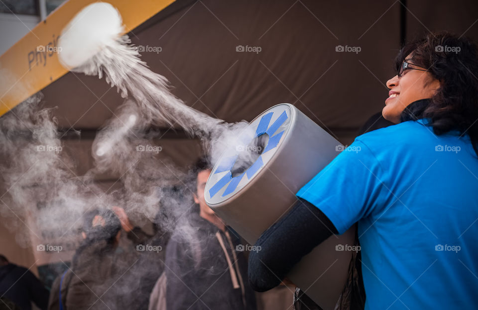 Lady demonstrating to public the use of low frequency sound waves to energetically propel a puff of smoke out of a barrel. Image captured at a local university's open day.