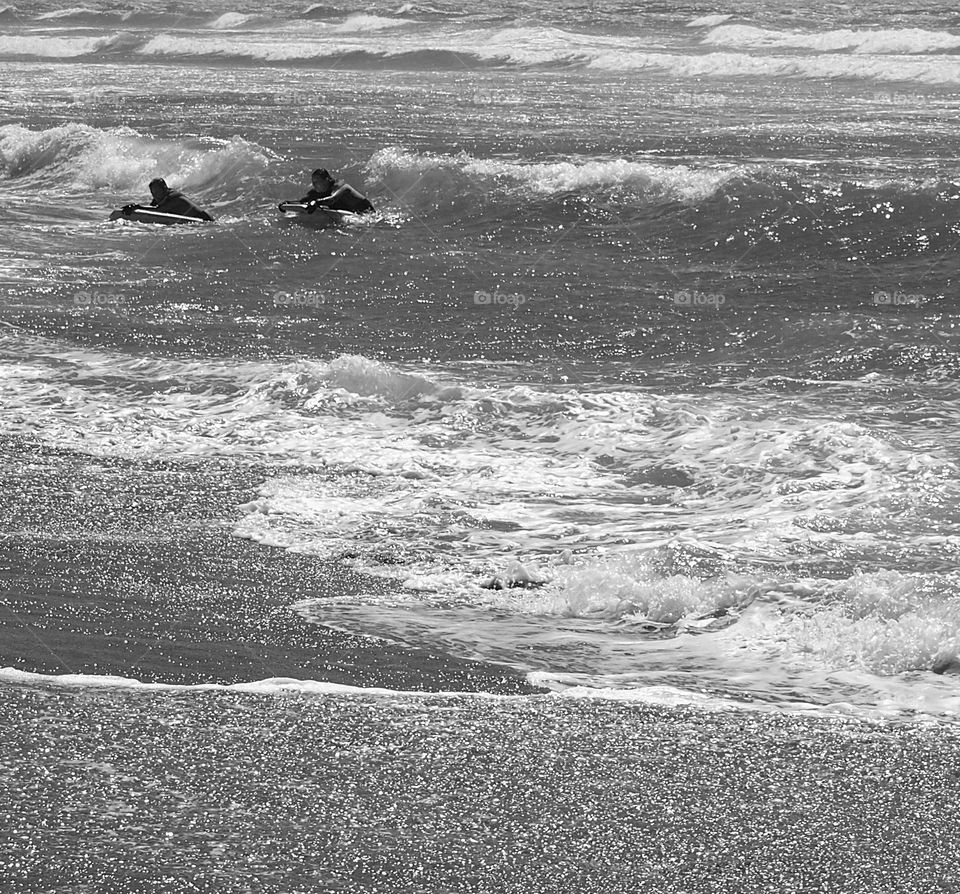 A pair of surfers nearly at the shore of rocky beach of the Pacific Ocean in Oregon on a summer day. 