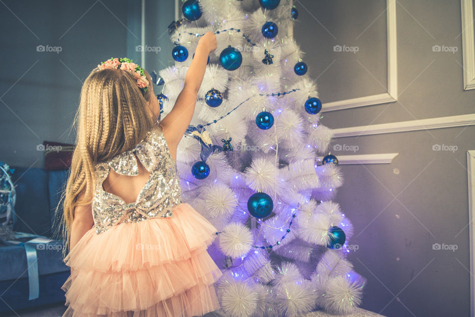 Little girl is hanging a toy on a tree