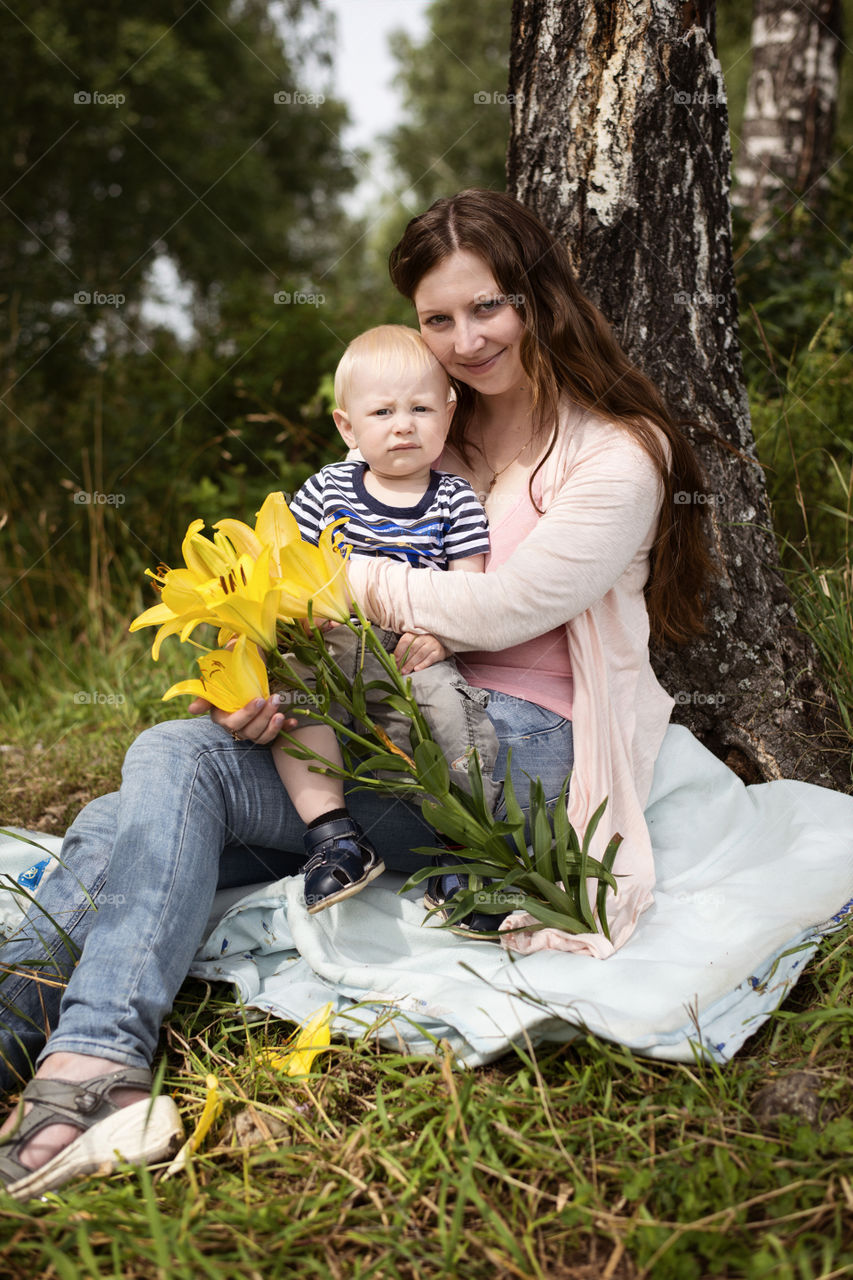 Woman with child sitting against tree with flowers