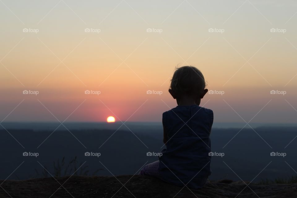 A child watching the sunset alone on a mountaintop 