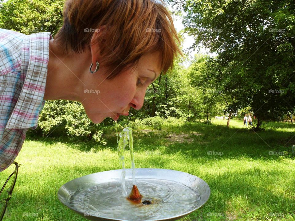 a girl is drinking water from a fountain
