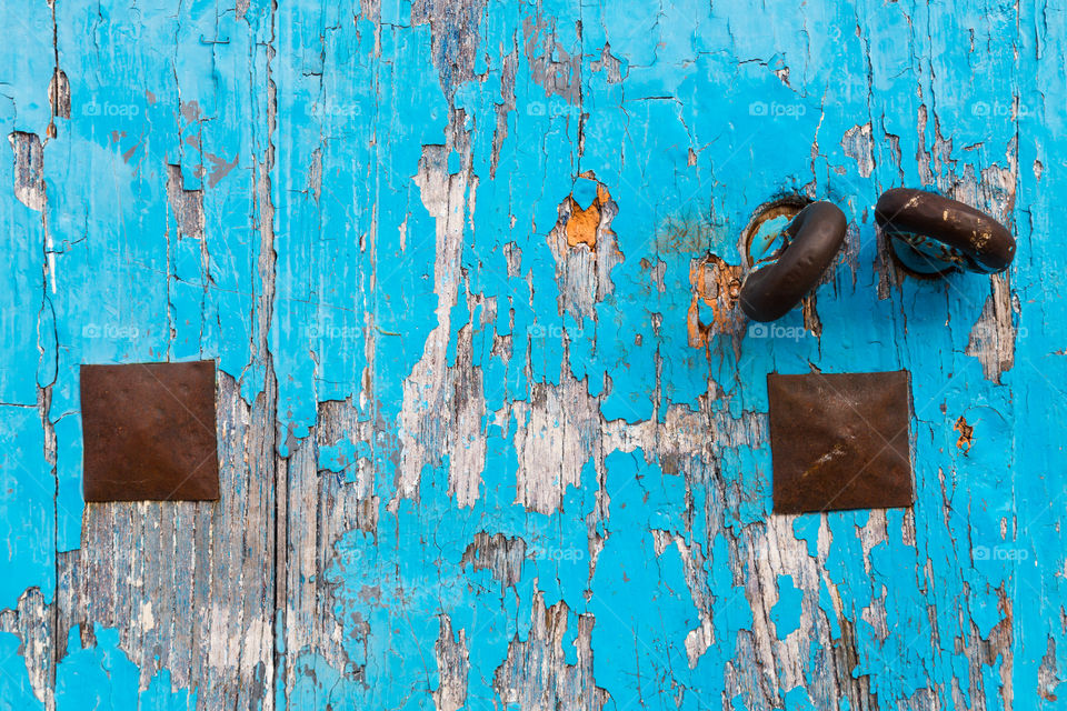 Worn blue wooden door. Old wooden door. Blue paint has chipped off from the door. Two copper rings and plates