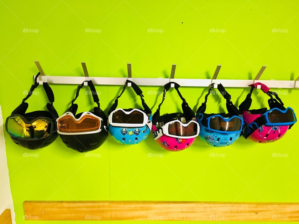 Ski helmets and goggles hanging on green wall