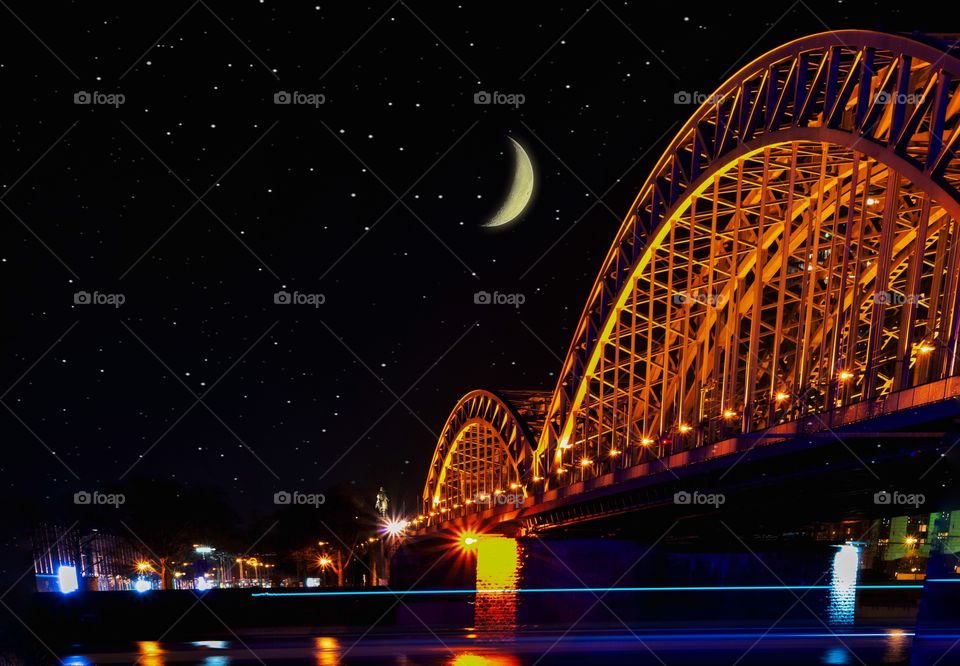 The steel Hohenzollern bridge crossing the Rhine river in the German city oh Cologne against a night sky