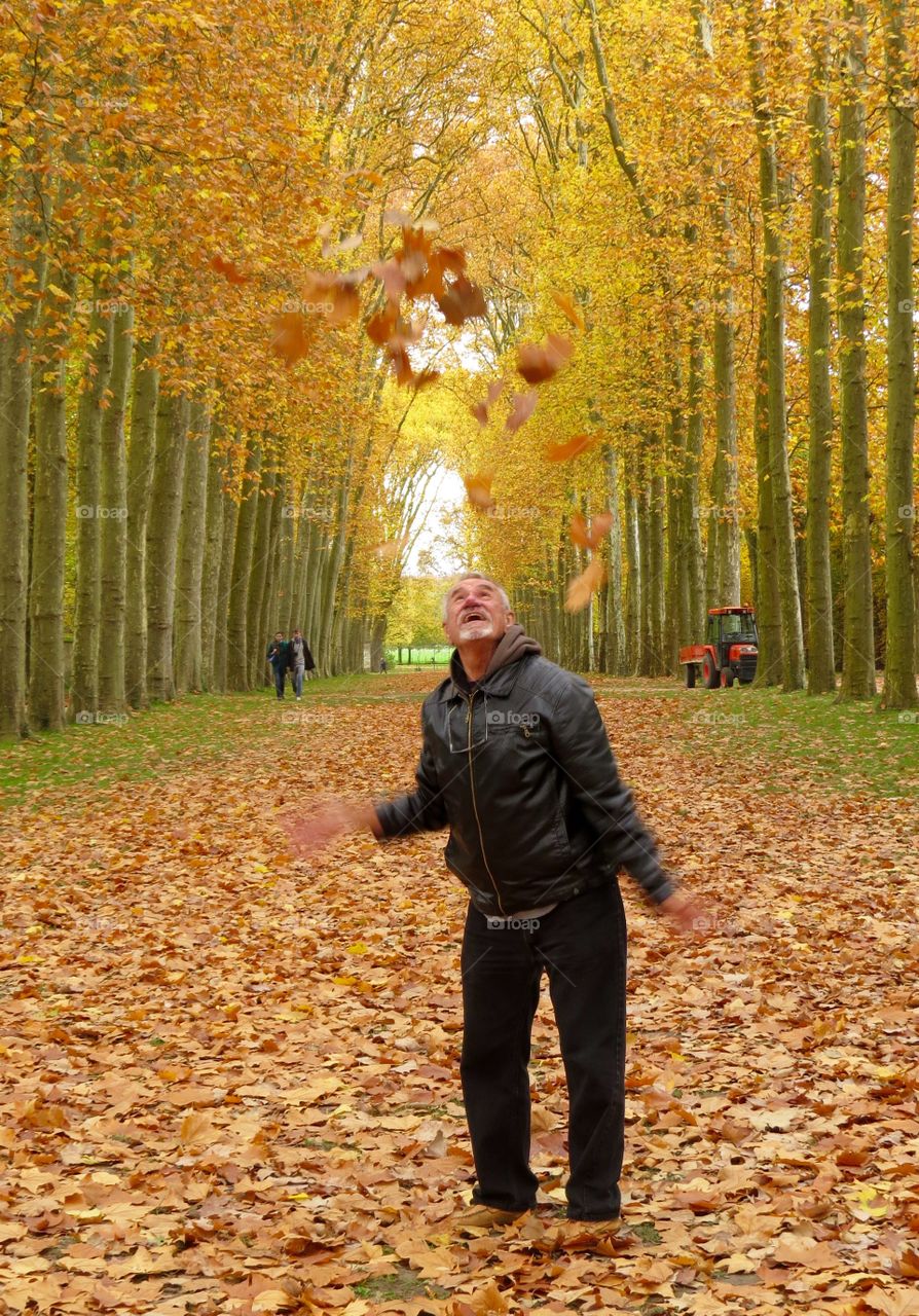 Senior man throwing dry leaves in air during autumn