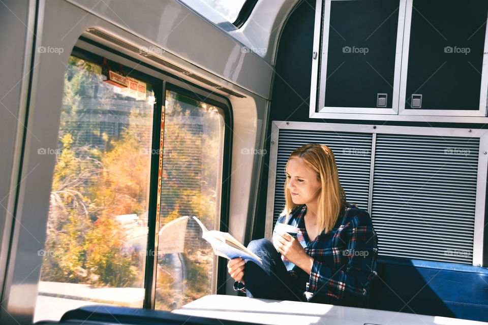 Woman traveling by train in USA and reading a book, drinking coffee 