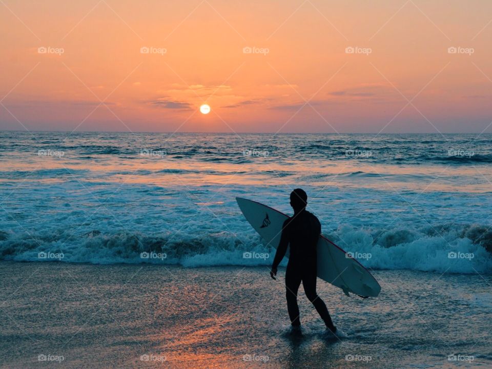 A surfer watches the ocean at sunset. 