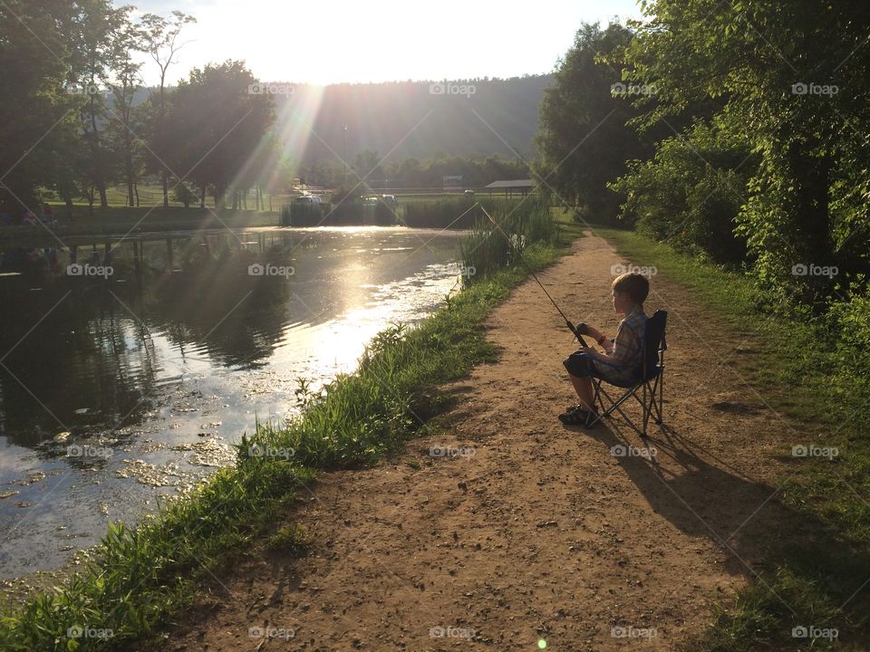 Child siting near riverside with fishing rod