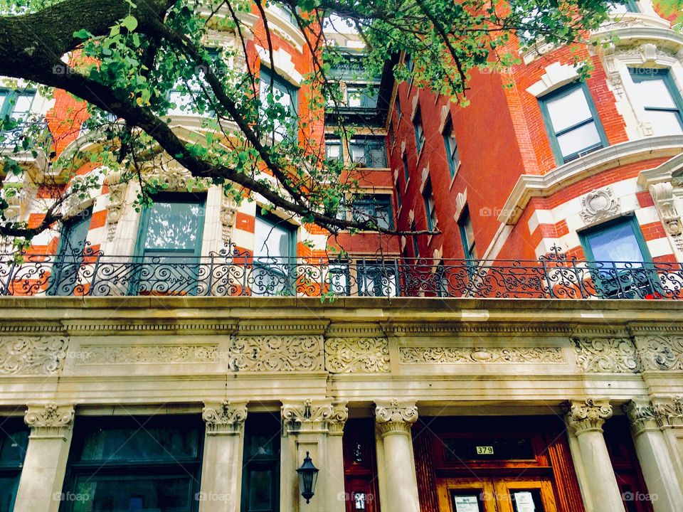 Fort Greene, Bklyn brownstone w eclectic detail: Ionic Greek columns, balconies w delicate iron cast designs on the railings, stucco ornamented window frames, half round offset building structures and a striped facade. 2019. Hypnotic Productions