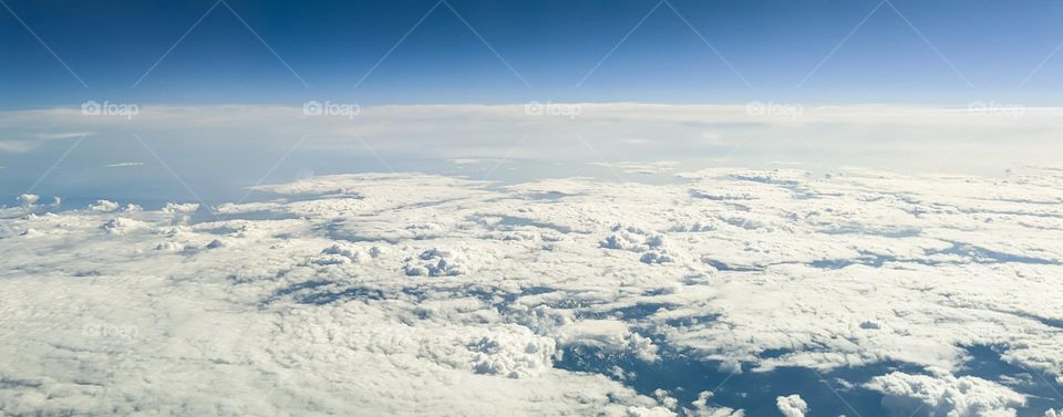 Beautiful natural wallpaper of white air clouds of bizarre shapes and sizes in the blue sky from an airplane height, close-up side view.