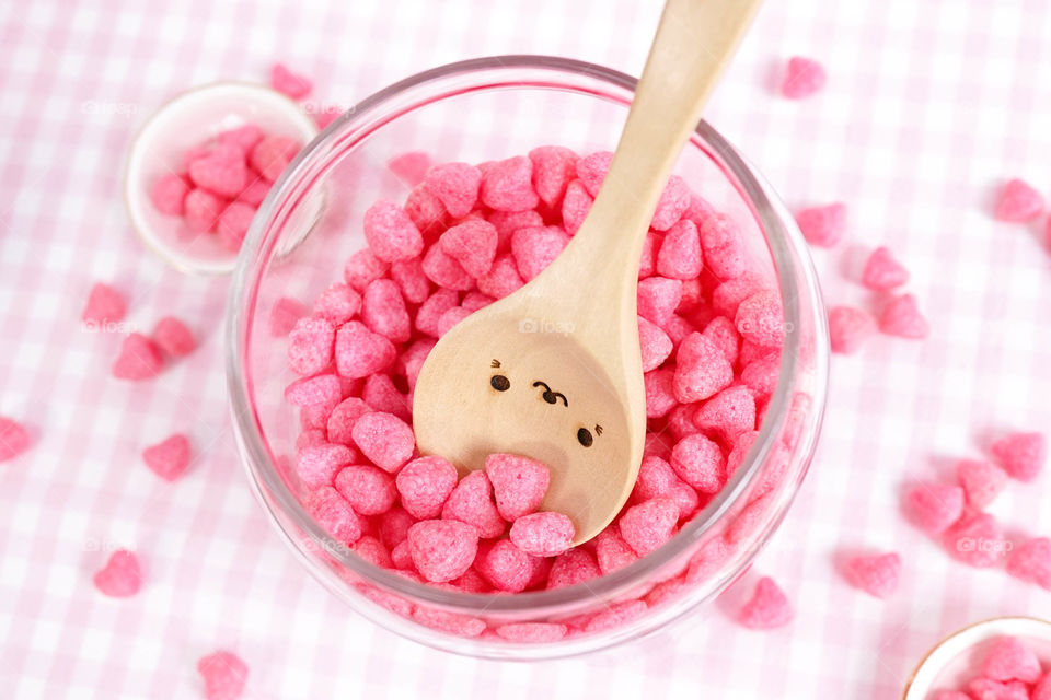 Bottle of love concept. A glass bottle with pink heart cereals and a cute wooden spoon.