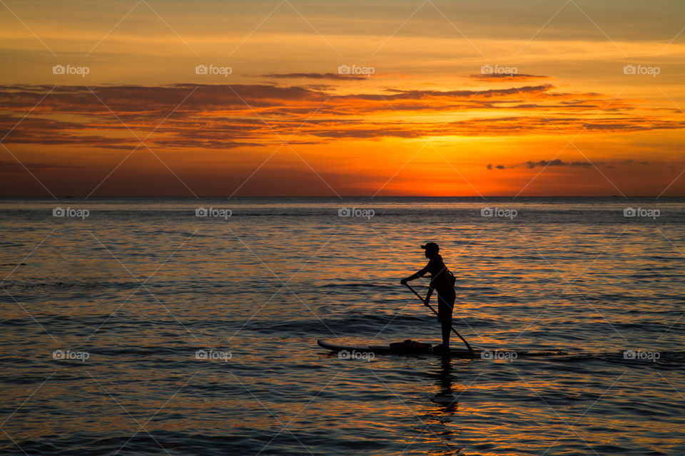 Silhouette of men on sup board on sunset 