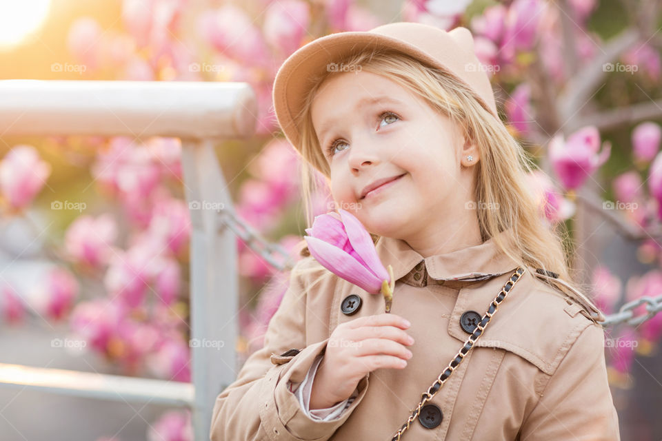 Cute little girl with blonde hair holding magnolia flower outdoor 
