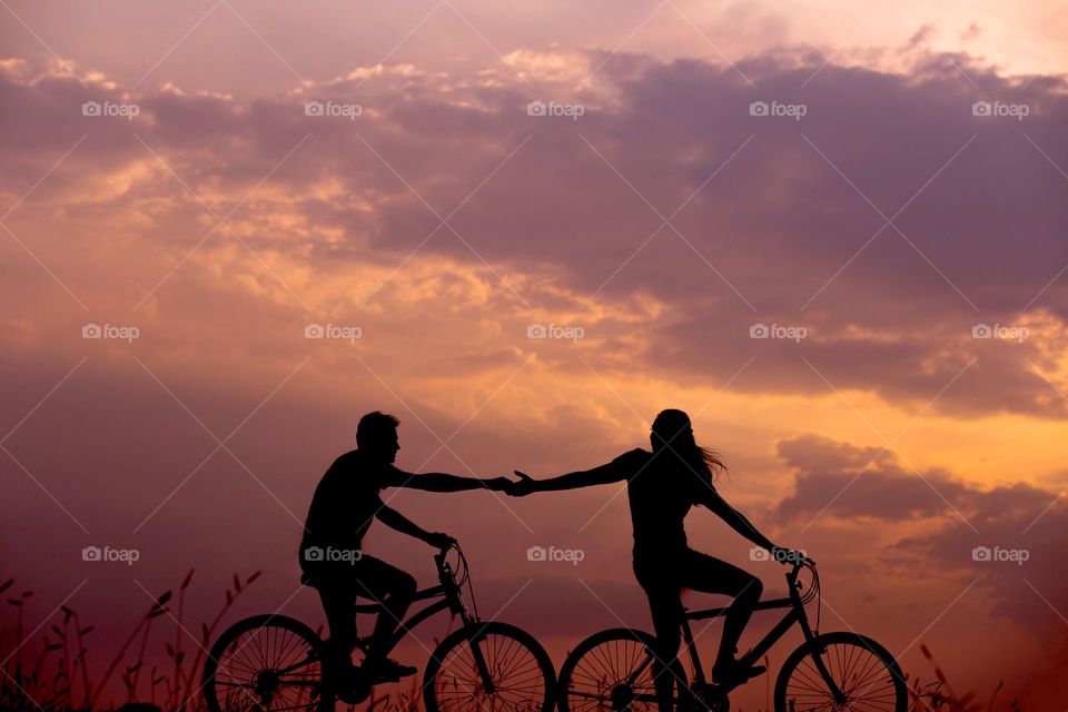 lovers share a silhouette bicycle ride, hands reaching out to each other