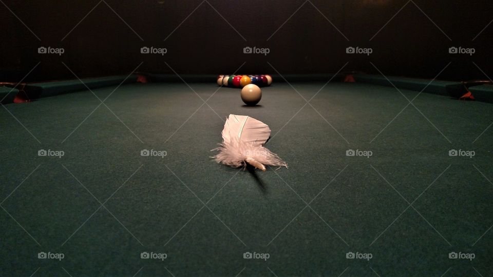 A dramatic shot of a feather in front of a set pool table as historic tradition amongst certain households was to hide feathers around the home.