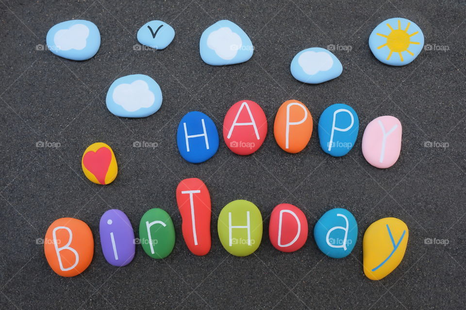 Creative Happy Birthday text with colored and carved sea stones over black volcanic sand