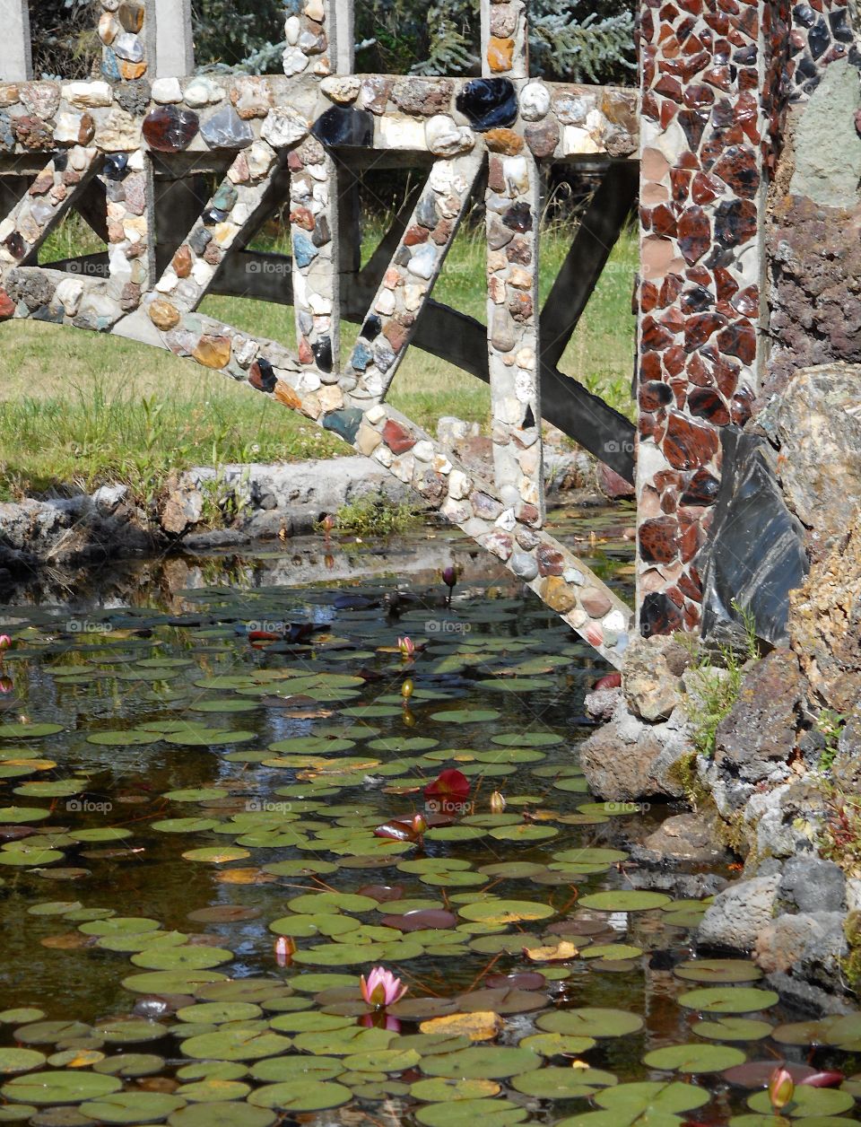 A beautiful and ornate rock bridge on a peaceful path crosses a fairytale style mote with lots of Lillie Pads at Peterson’s Rock Garden on a sunny summer day in Central Oregon. 