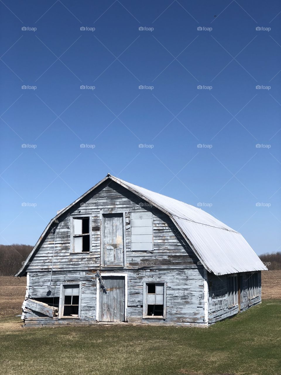 Light Blue Abandoned Barn with a Clear Sky and Field in the Background. 