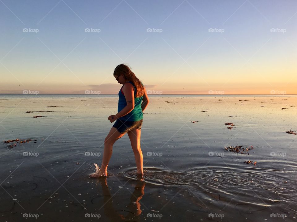 Young girl wading in water ocean at low tide at sunset