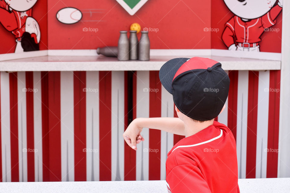 Monochromatic image of a young boy wearing red and throwing a ball at a red carnival game