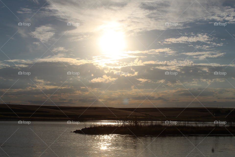 Sun in Clouds Reflecting on Lake with Land in background