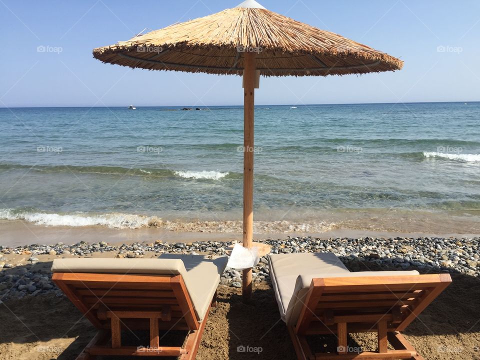 Two sunbeds and a thatch umbrella on the beach in Crete
