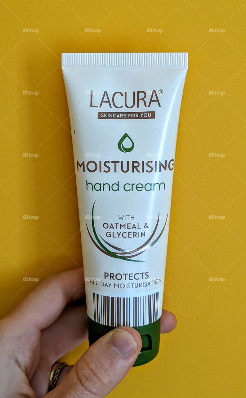 a tube of lacura moisturizing hand cream being held against a bright yellow wall