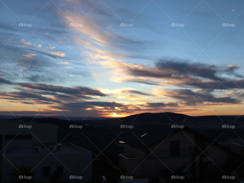 Blue sky with dark grey and bright yellow clouds and yellow Sun