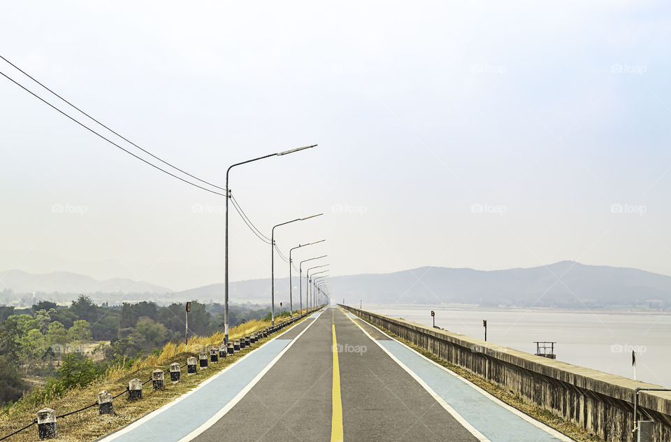 The road on the dam Background mountains and water at Krasiew dam ,Supanburi Thailand.