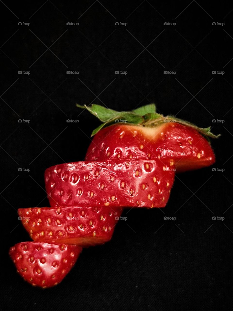 Food.  Fruits.  On a black background, red strawberries, which are cut into circles and folded in the form of a ladder