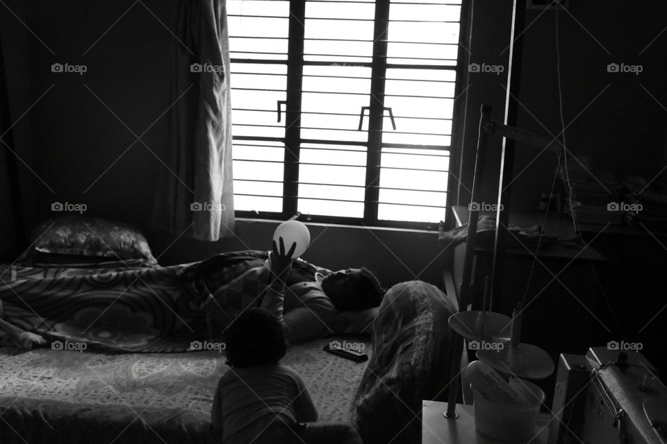I have taken a black and white photography. I tried to create haunted environment. One lady is lying down on a bed in a room with a balloon and a child standing beside her bed.