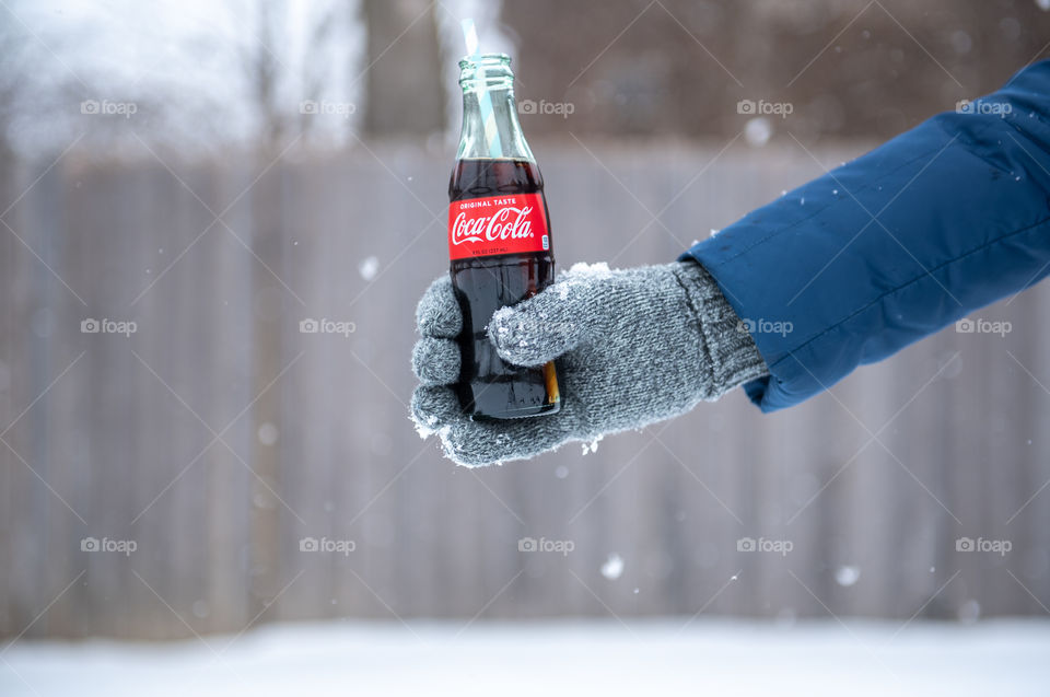 Person's gloved hand holding out a bottle of Coca-cola outdoors in the snow