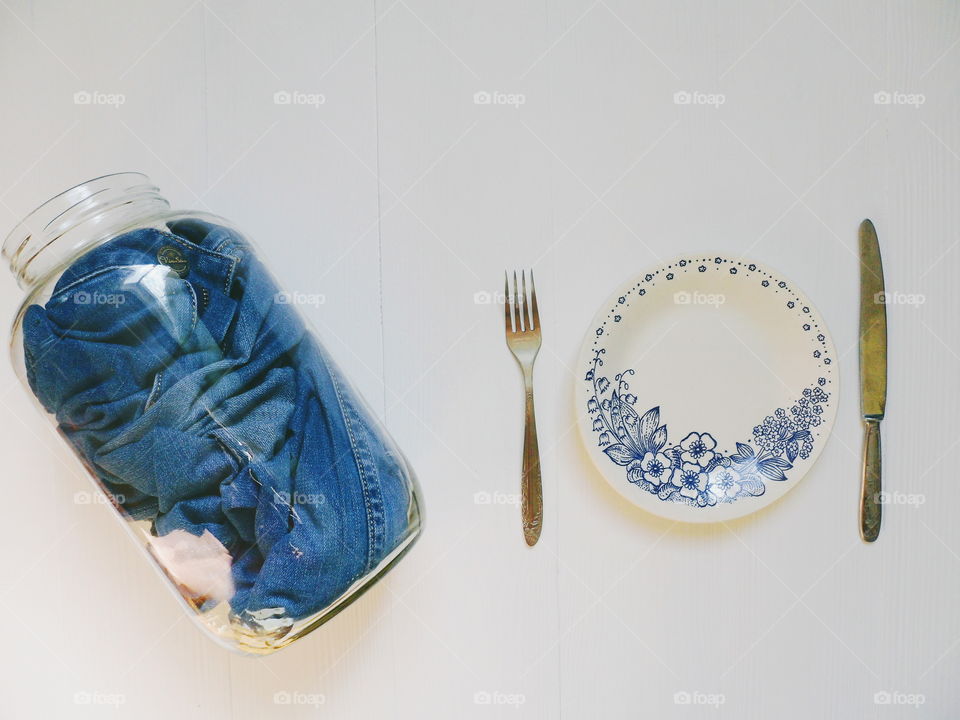 in a glass jar men's jeans pants and a plate with a fork and knife on a white background