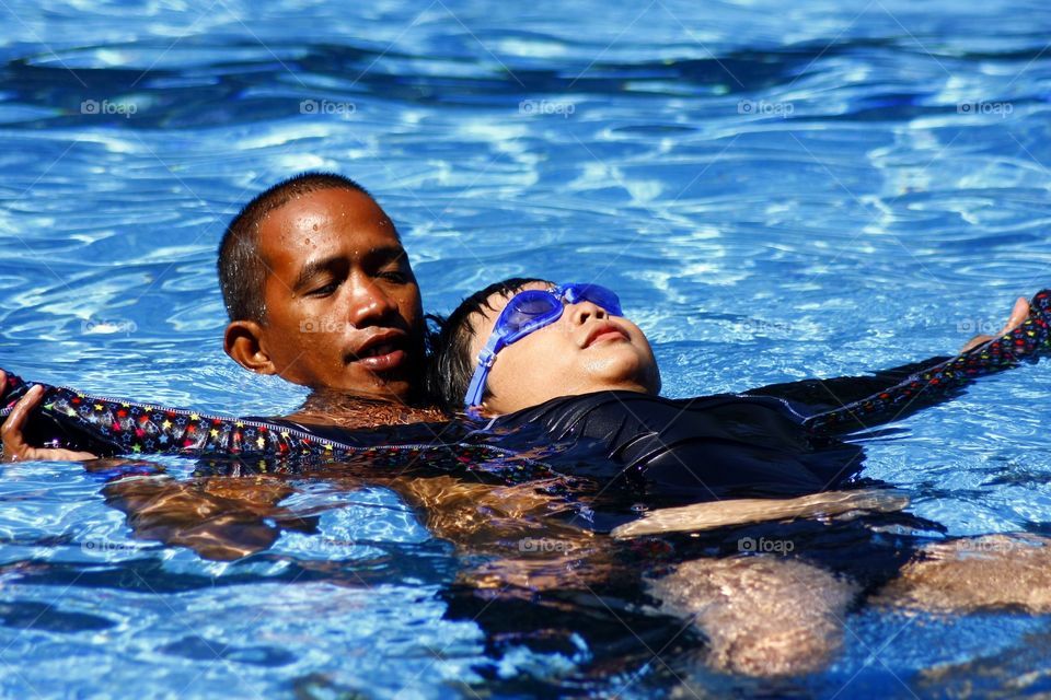 young kid learns how to float on his back with the help of a swimming coach