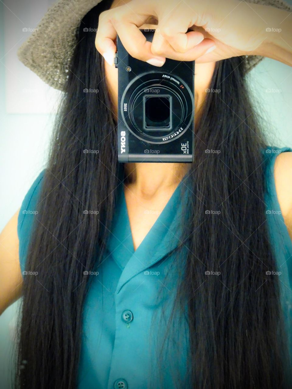 A woman with a black long hair holding a point and shoot camera.