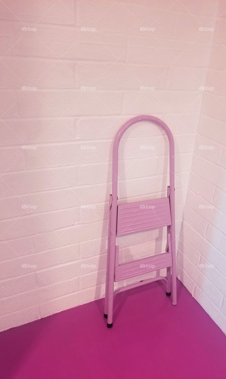 Old pink step ladder leaning against a white brick wall.