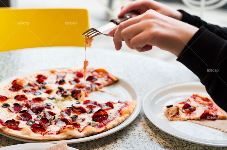 Girl's hands taking a melted cheese from a pepperoni pizza in a cafe.