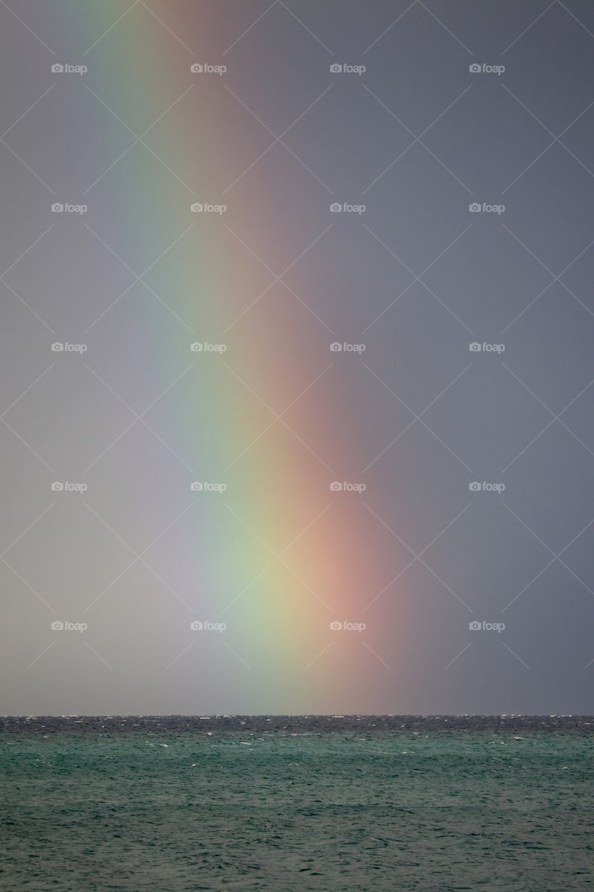 Bright rainbow on the horizon of a dark choppy sea during a storm 