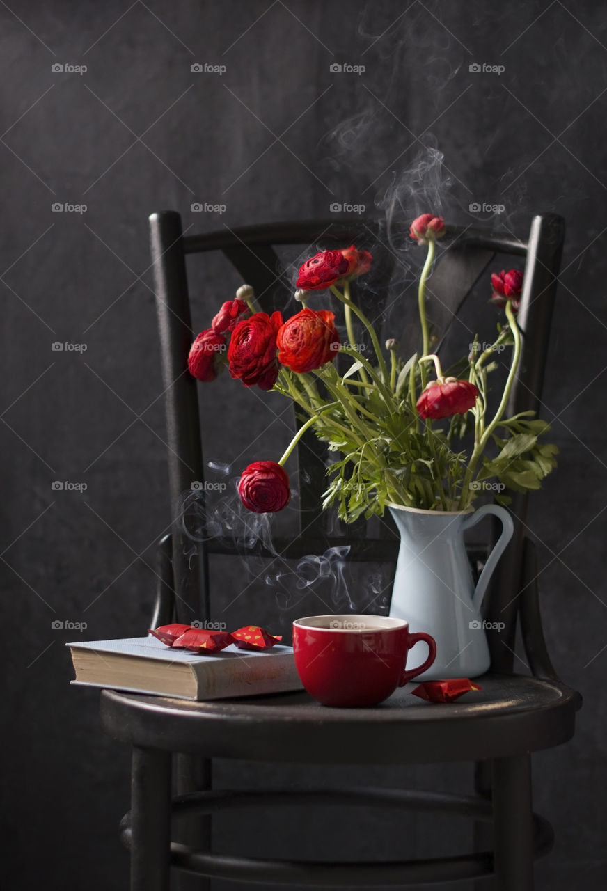coffee in a red porcelain cup and a book on the background of a jug with ronunculus, a photograph in a dark key on a black background