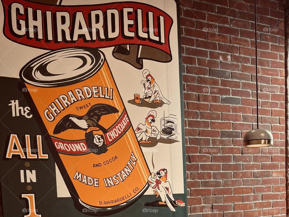 Vintage Ghirardelli Chocolate sign on an old brick wall with a light hanging down.