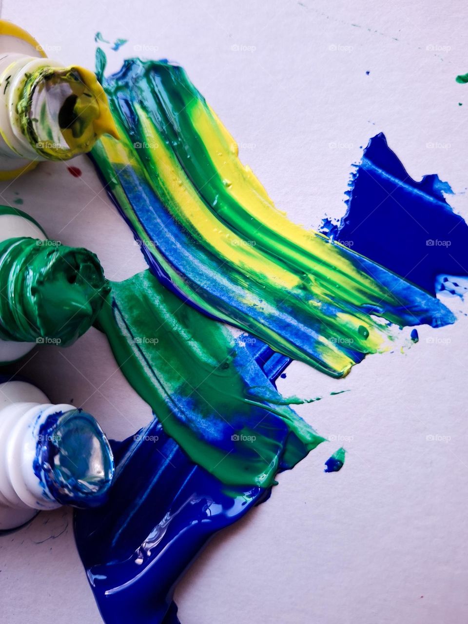 brushstrokes of different colors, namely yellow, blue and green, on a white canvas