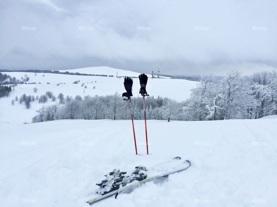 Skis in the snow with black gloves over ski poles surrounded by winter scenery